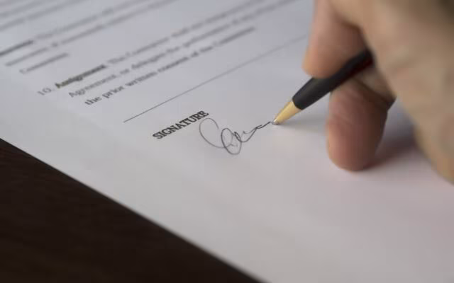 Dłoń podpisuje dokument długopisem na linii oznaczonej podpisem