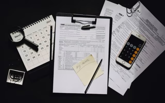 Formularze podatkowe, kalendarz i telefon rozłożone na biurku podczas rozliczenia