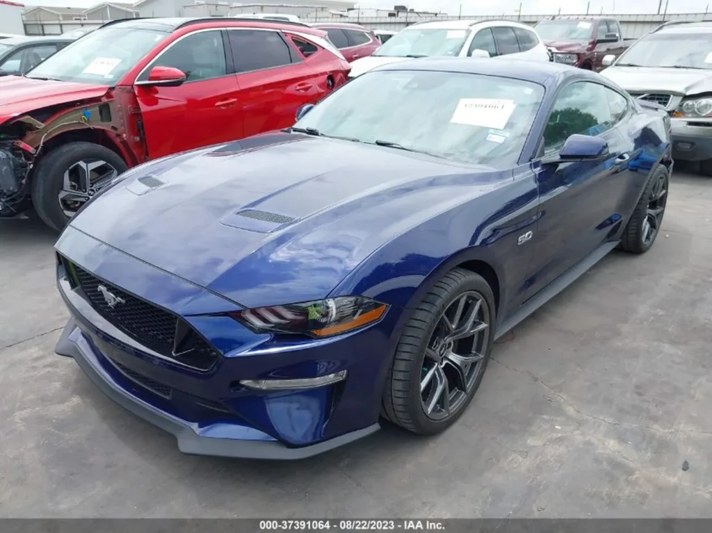 Niebieski Ford Mustang GT – ujęcie 3/4 z przodu po lewej, parking aukcyjny.