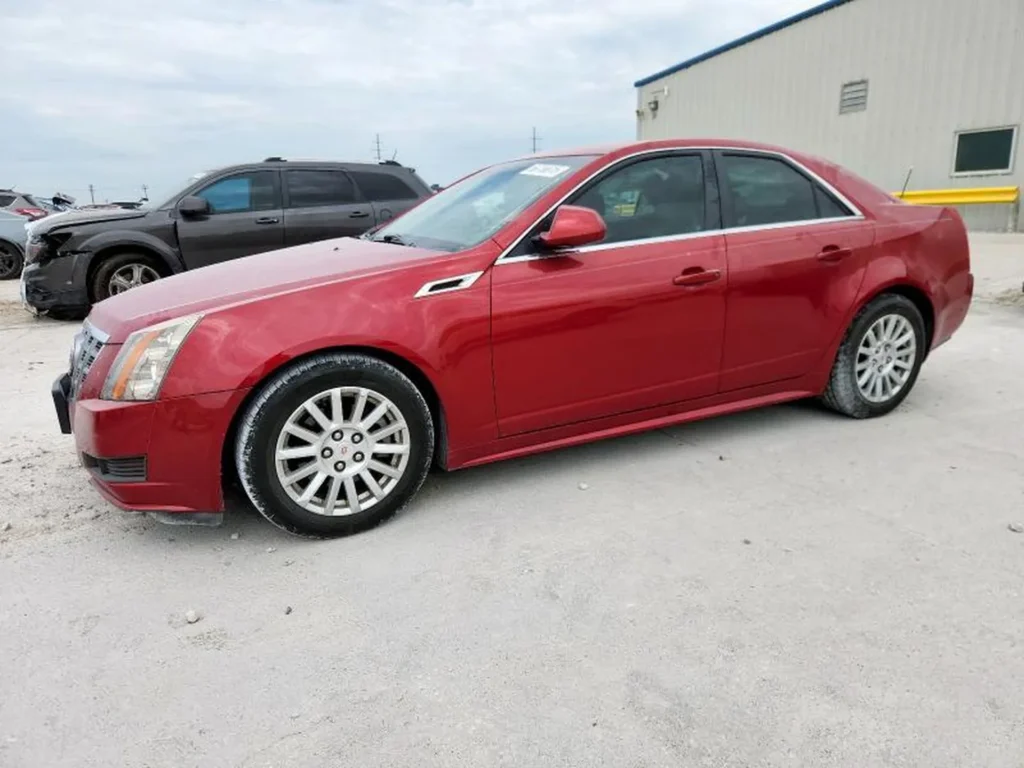 Czerwony Cadillac CTS sedan z boku z lewej, auto stoi na żwirowym placu.