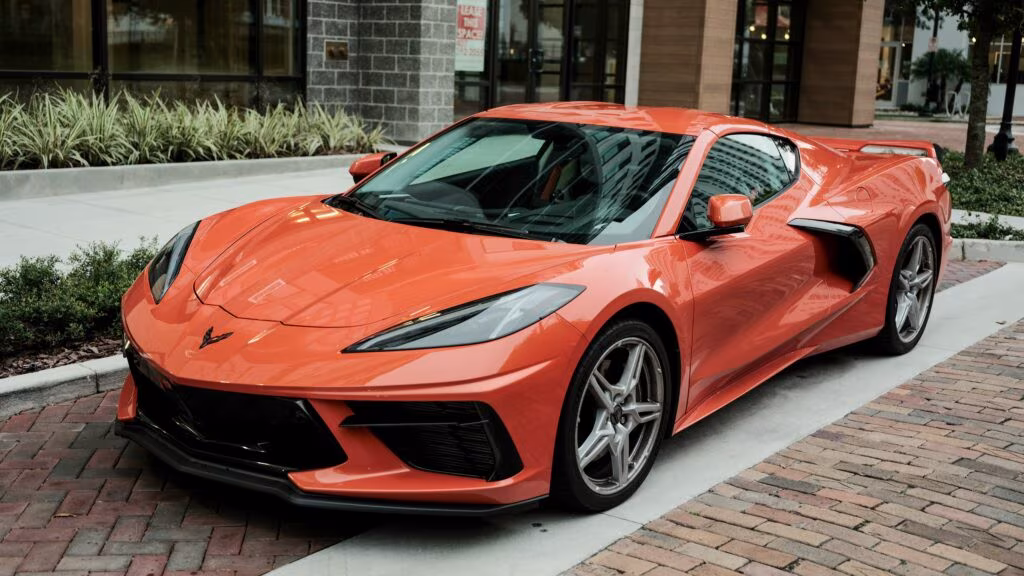 Pomarańczowe Chevrolet Corvette C8 zaparkowane na chodniku przy nowoczesnym budynku, widok z przodu i boku