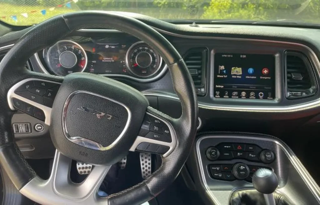 Kokpit Dodge Challenger – kierownica SRT, zegary analogowe, ekran Uconnect, manualna dźwignia zmiany biegów.