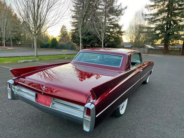 Bordowy Cadillac coupe od tyłu, długie płetwy i chromowane zderzaki, spokojny plener.