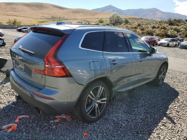 Srebrne Volvo XC60, ujęcie tylno-boczne na żwirowym placu, w tle wzgórza.