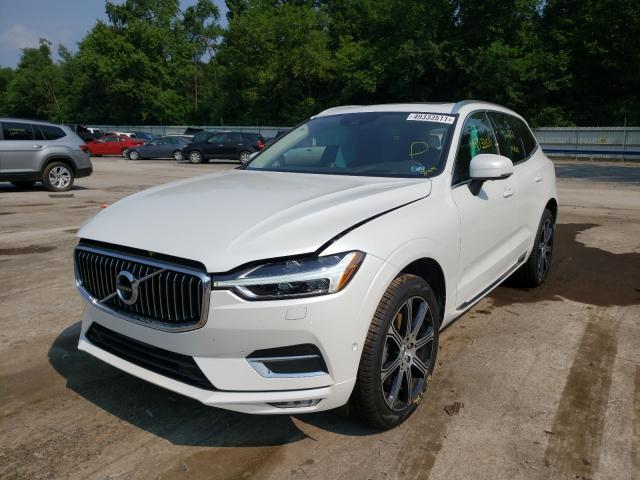 Białe Volvo XC60 z lekko uniesioną maską, ujęcie z przodu na placu.