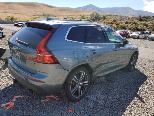 Srebrne Volvo XC60, ujęcie tylno-boczne na żwirowym placu, w tle wzgórza.