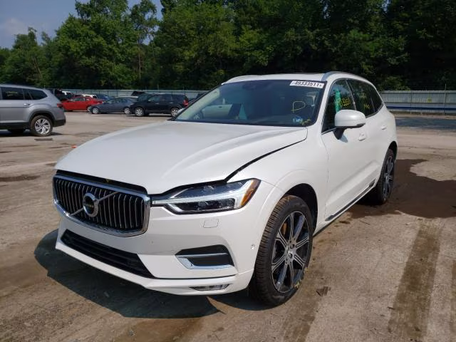 Białe Volvo XC60 z lekko uniesioną maską, ujęcie z przodu na placu.