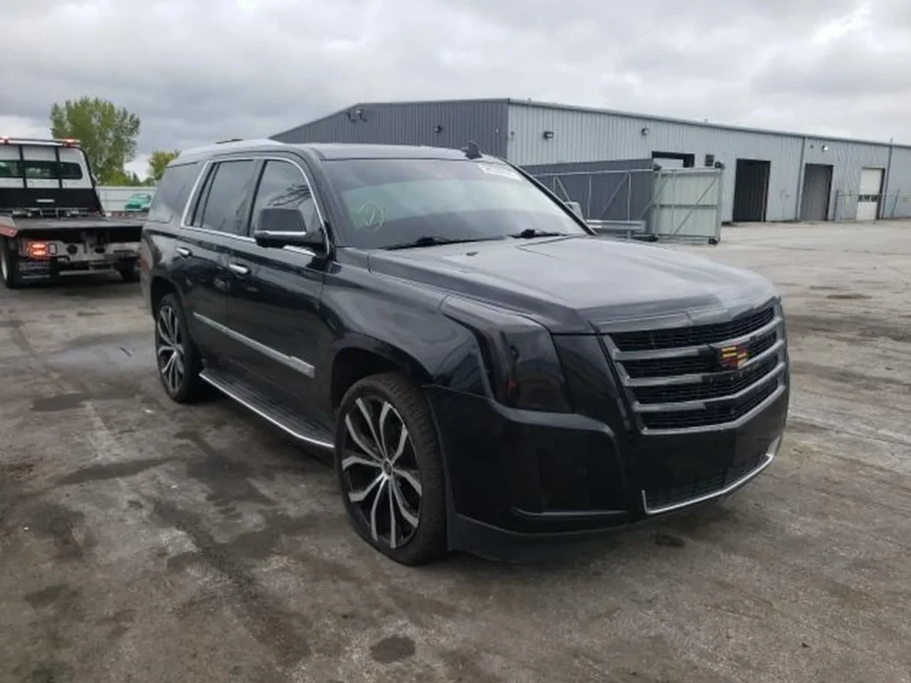 Czarny Cadillac Escalade z przodu z lewej, duże felgi, plac przy magazynach.
