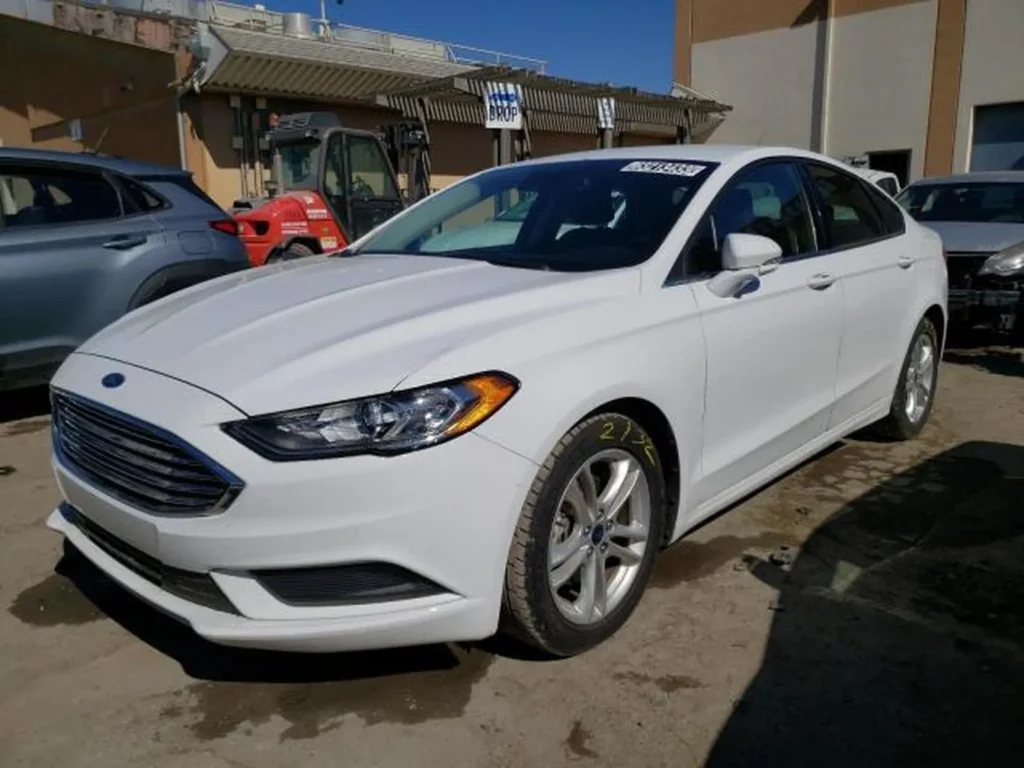 Biały Ford Fusion (2018) – widok z przodu/lewego boku na placu, reflektory LED i chromowany grill.
