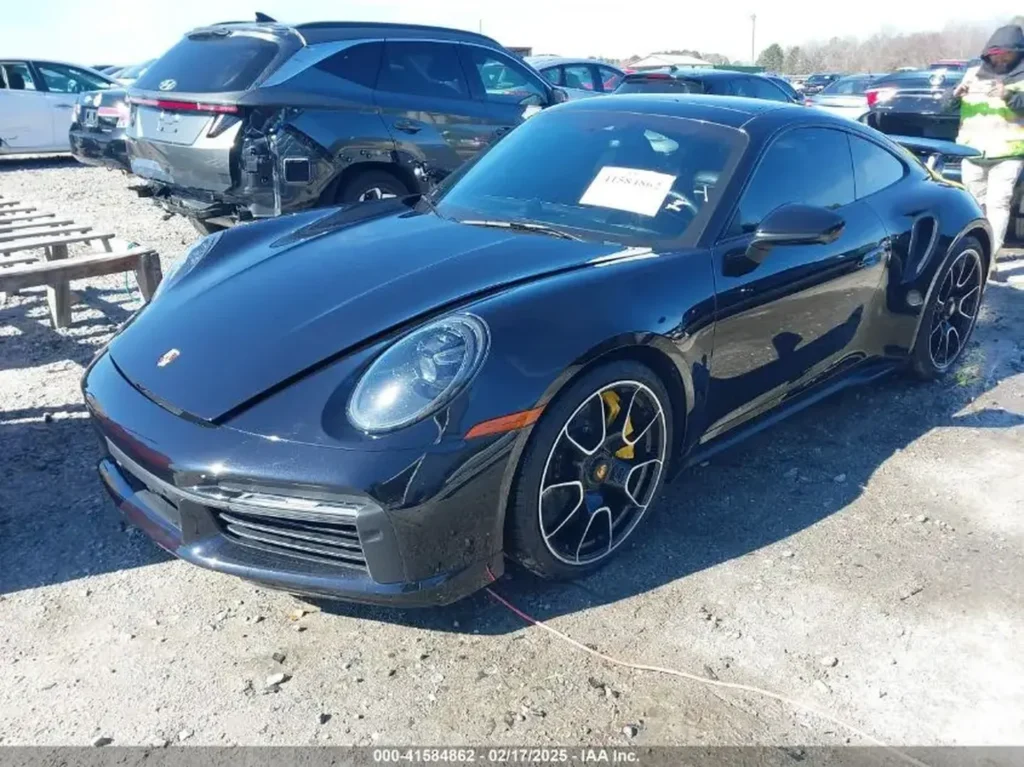Czarny Porsche 911 Turbo S (992) – ujęcie z przodu z lewej; lekko uchylona maska, zarysowania i ubytki na dolnym zderzaku.