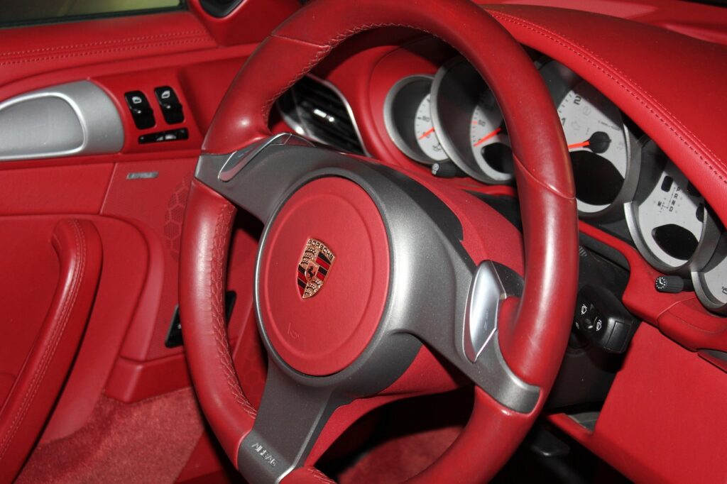 Wnętrze Porsche z czerwonym skórzanym wykończeniem, kierownicą z logo marki i klasycznymi zegarami na desce rozdzielczej.