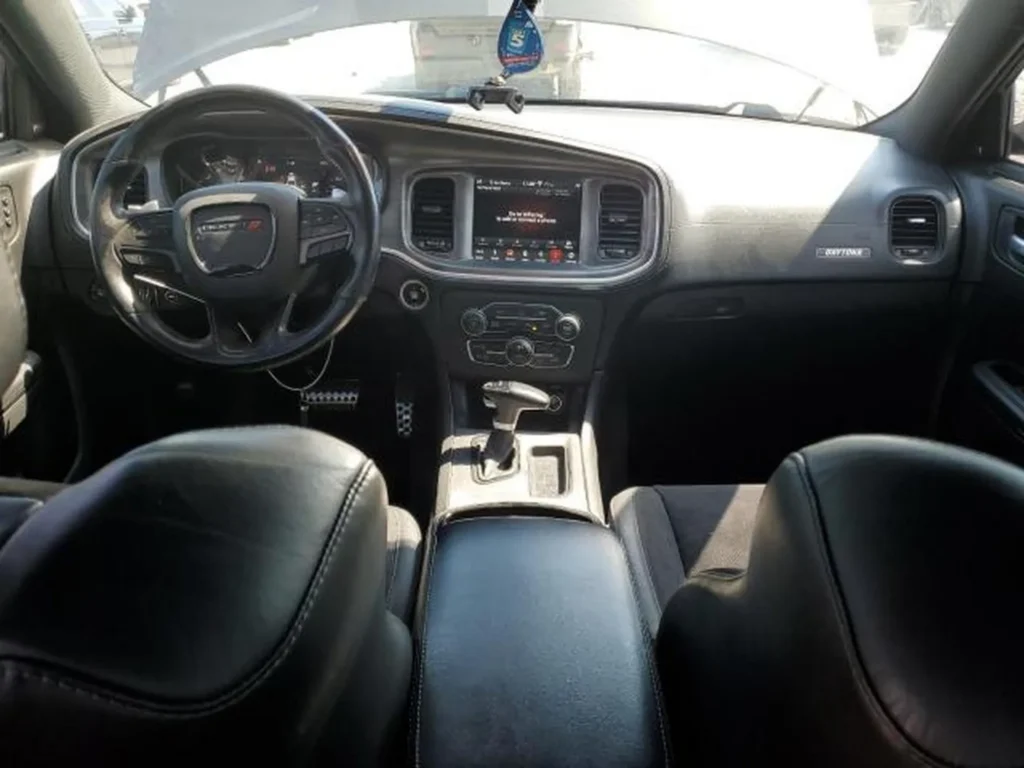Wnętrze Dodge Chargera Daytona – czarna skóra/alcantara, kierownica z logo, ekran multimedialny i automat na konsoli.