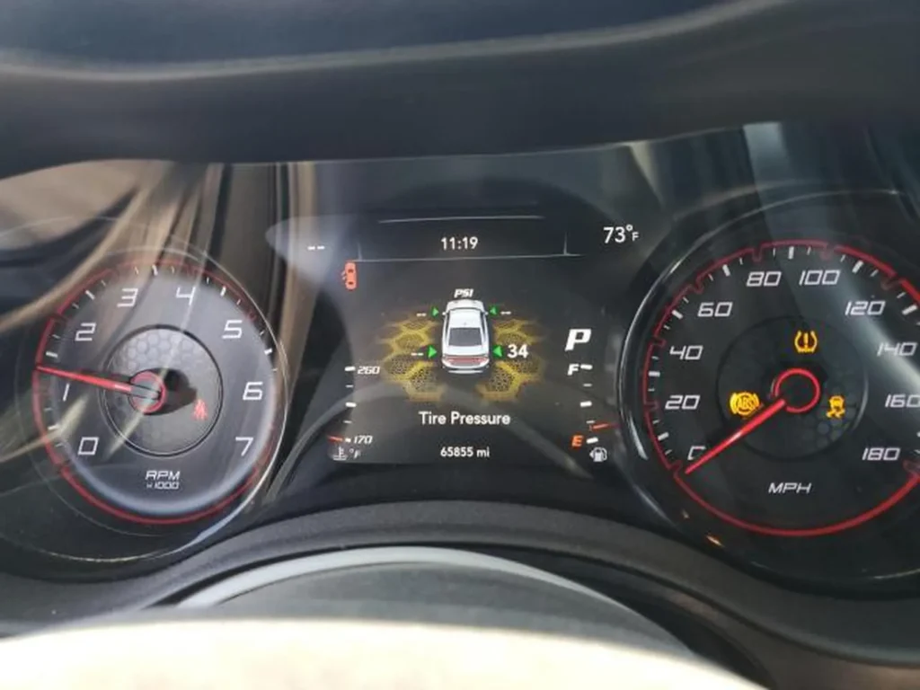 Zbliżenie zegarów Dodge Chargera; ekran pokazuje ciśnienie w oponach (34 PSI) i przebieg 65 835 mil, świecą się kontrolki TPMS/ESP.