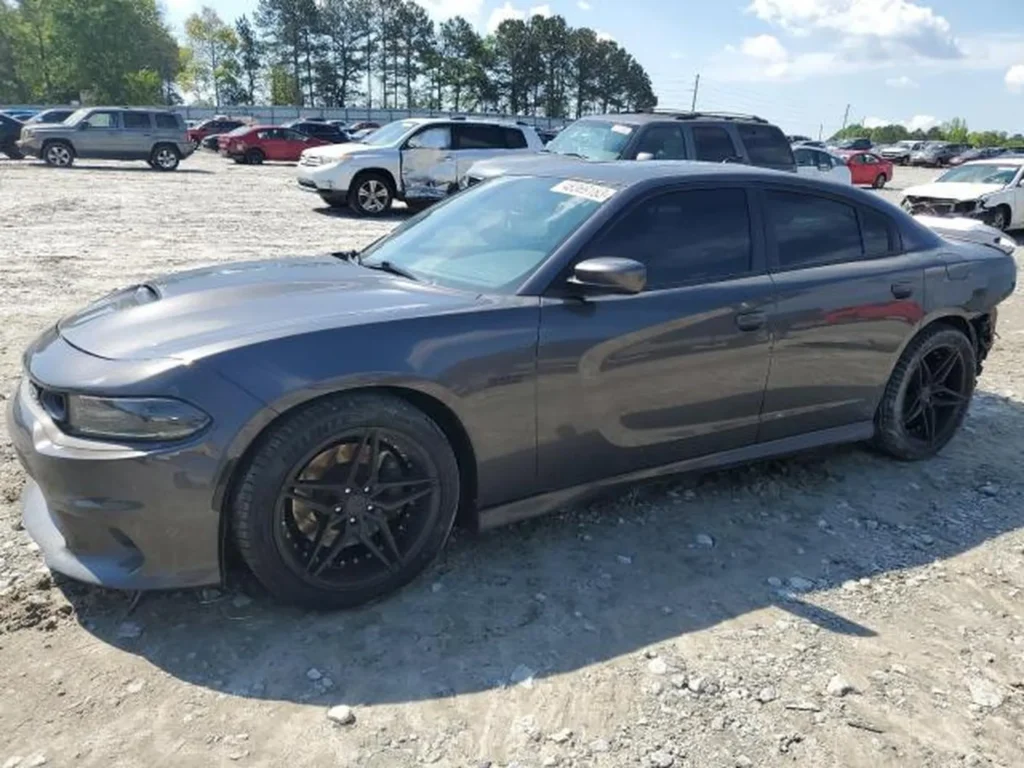 Lewy bok szarego Dodge Chargera Daytona na żwirowym placu; ciemne, wieloramienne felgi.
