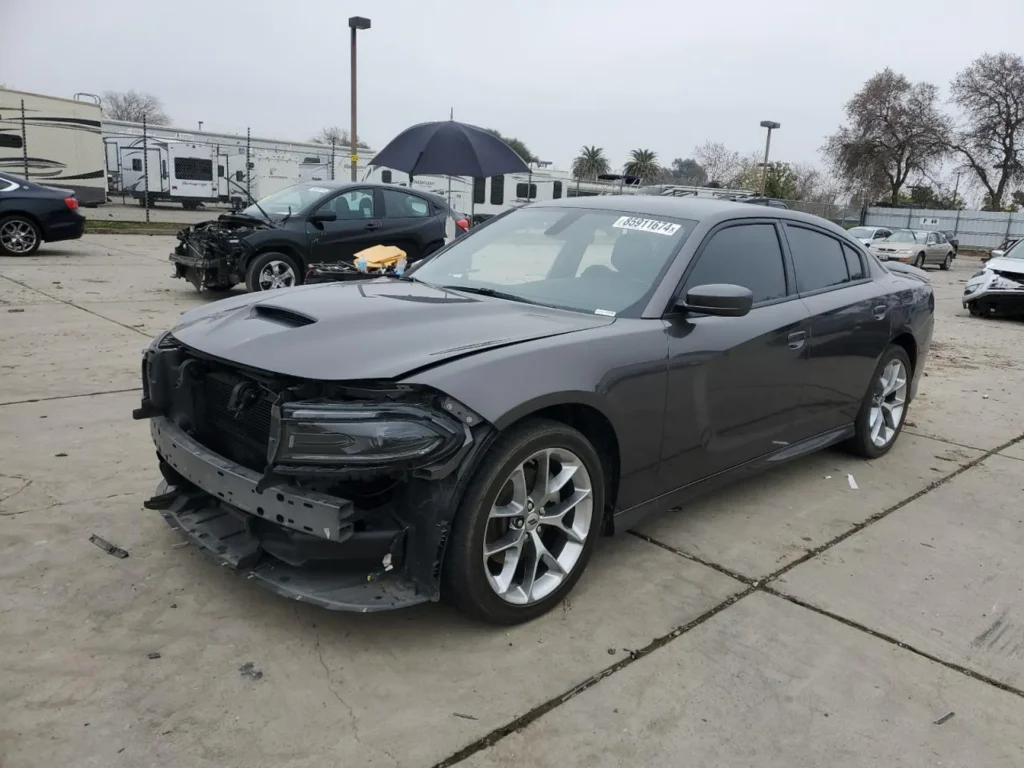 Szary Dodge Charger z uszkodzonym przodem i zdemontowanym zderzakiem, widok z przodu z lewej strony.
