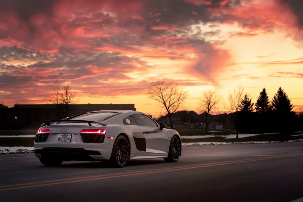 Białe Audi R8 jadące po drodze o zachodzie słońca, z dynamicznym designem i sportowym spoilerem.