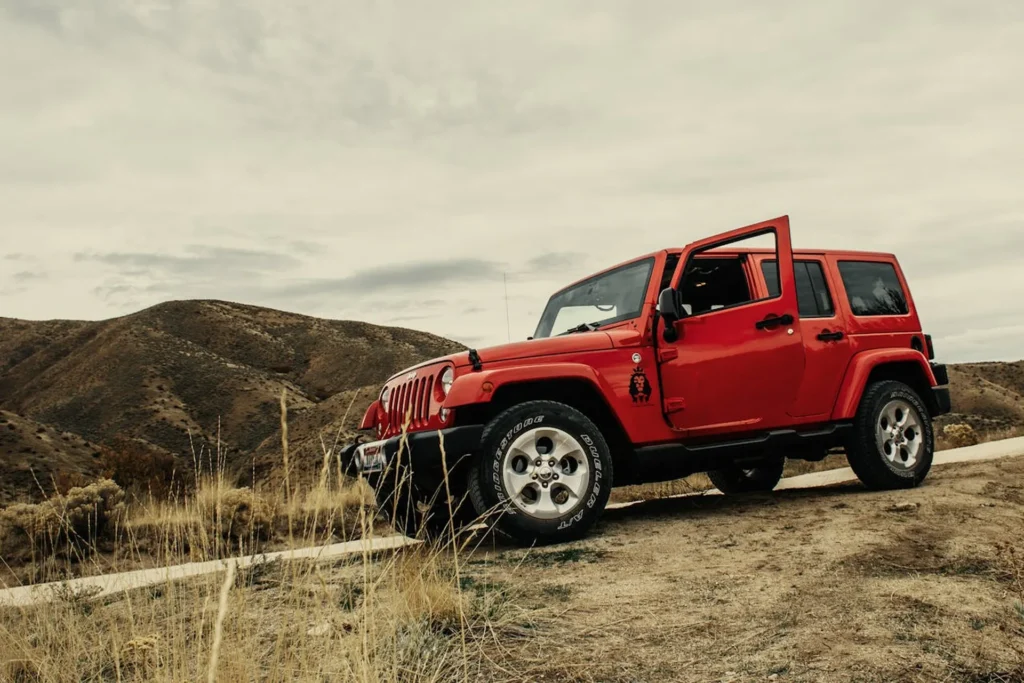 Czerwony Jeep Wrangler zaparkowany na górskiej drodze, z otwartymi drzwiami, gotowy na terenową przygodę.