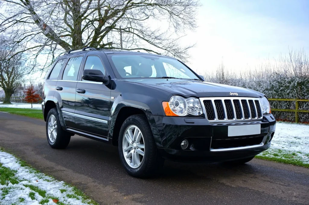 Czarny Jeep Grand Cherokee zaparkowany na wiejskiej drodze w zimowym krajobrazie, z lekko ośnieżonym otoczeniem.