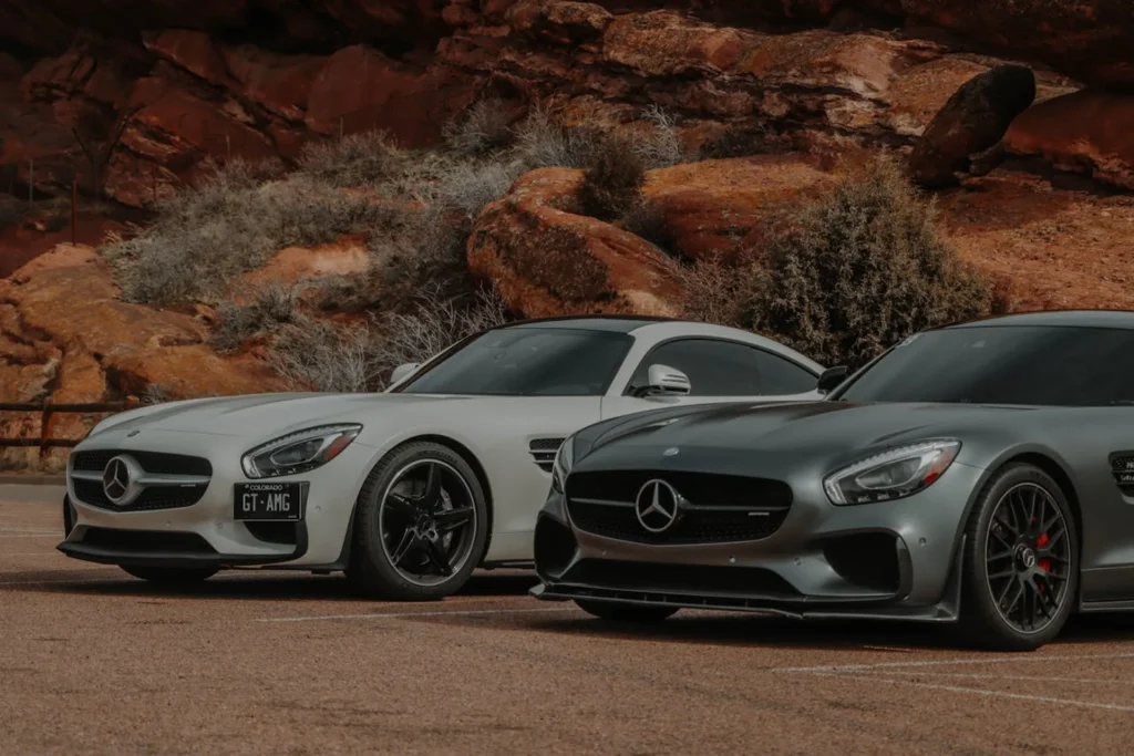 Dwa Mercedesy AMG GT – biały i szary – zaparkowane na tle czerwonych skał, podkreślające luksus i sportowy charakter marki.