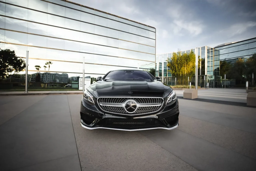 Czarny Mercedes-Benz zaparkowany przed nowoczesnym, szklanym budynkiem, z imponującym grillem i refleksami światła na karoserii.