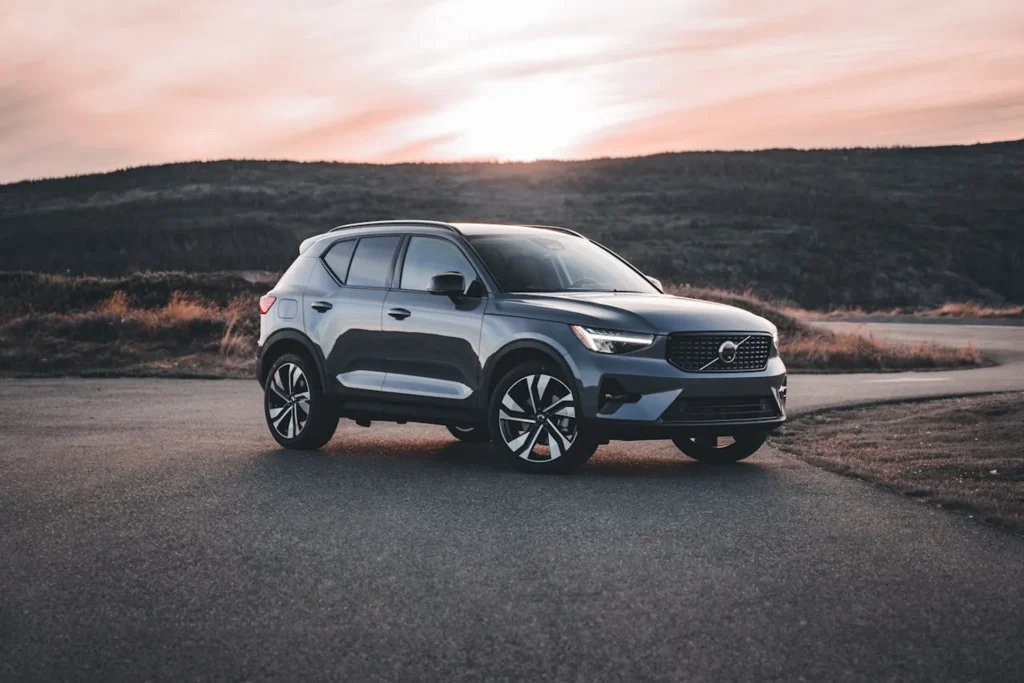 Volvo XC40 w kolorze szaro-niebieskim zaparkowane na drodze o zachodzie słońca, na tle malowniczego krajobrazu z wzgórzami i otwartą przestrzenią.