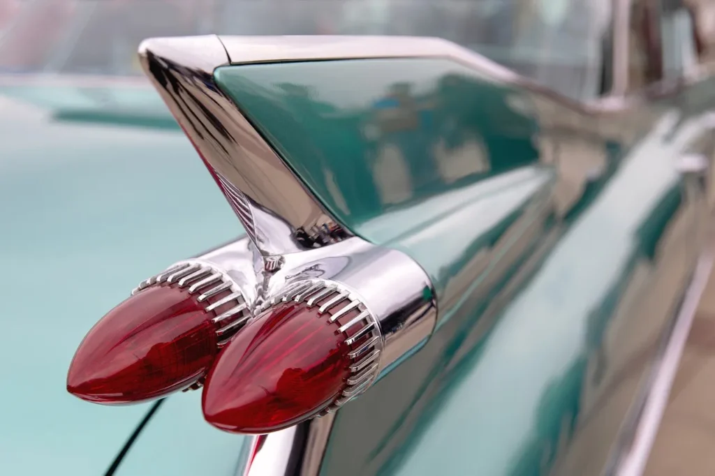 Zbliżenie na tylną płetwę i charakterystyczne podwójne czerwone światła Cadillaca z końca lat 50., z chromowanymi detalami i zielonym lakierem karoserii.