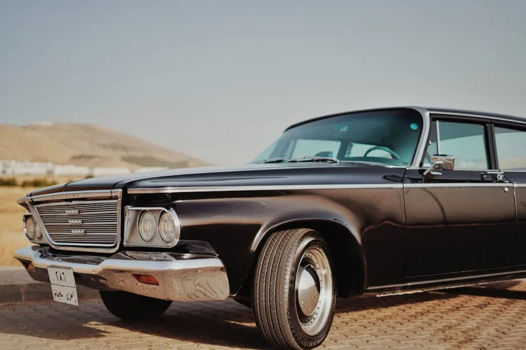 Czarny klasyczny Chrysler z lat 60. zaparkowany na tle górskiego krajobrazu, z masywnym grillem i charakterystycznym designem.