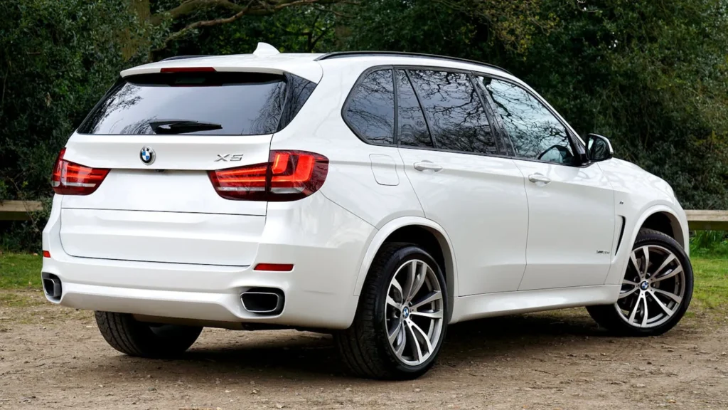 Tylny widok białego BMW X5 zaparkowanego w lesie, z widocznymi reflektorami i oznaczeniem modelu