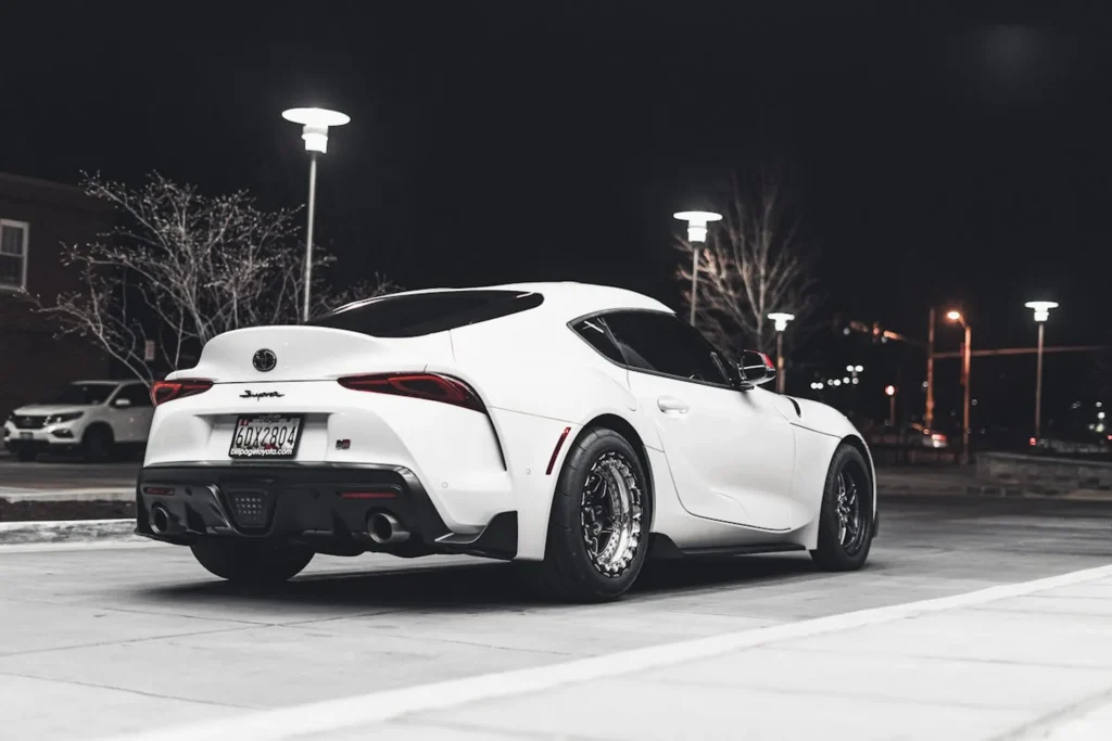 Biała Toyota Supra GR zaparkowana nocą pod lampami ulicznymi, widok z tyłu