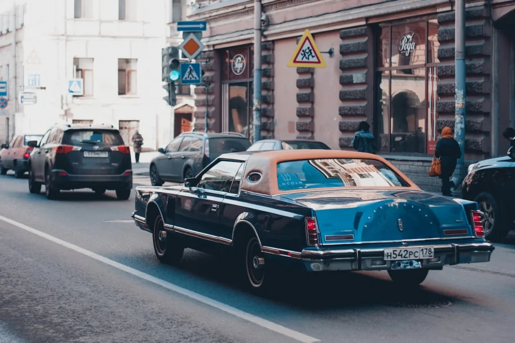 Niebieski Lincoln Continental Mark V z brązowym dachem vinilowym jadący ulicą w centrum miasta