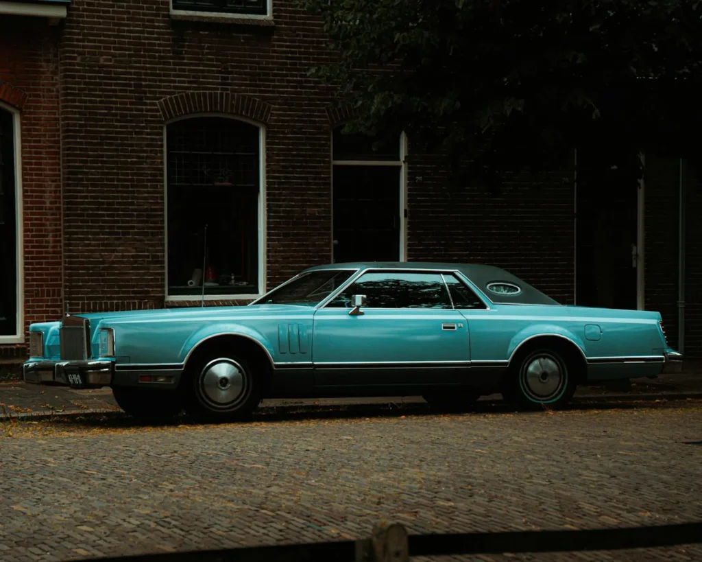 Turkusowy klasyczny Lincoln Continental Mark V zaparkowany na brukowanej ulicy przed kamienicą
