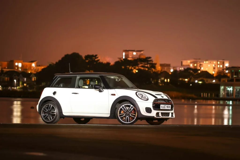 Stylowy Mini Cooper z USA sfotografowany nocą na tle oświetlonego miasta – dynamiczne ujęcie podkreślające miejski charakter auta.