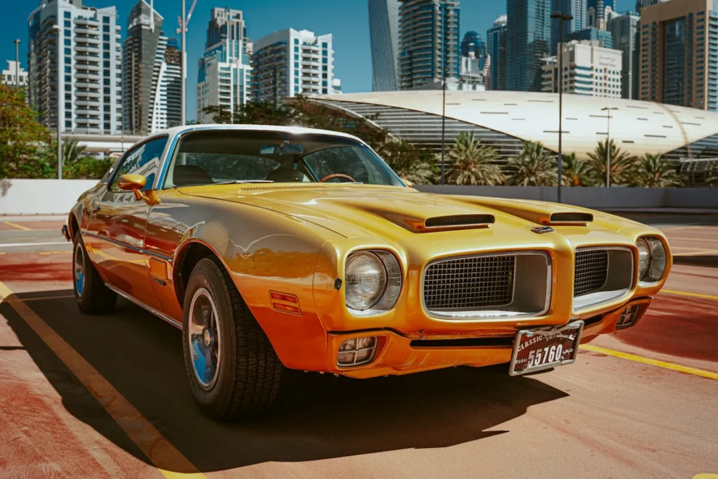 Złoty Pontiac Firebird Trans Am z USA drugiej generacji zaparkowany w słoneczny dzień na tle nowoczesnych wieżowców