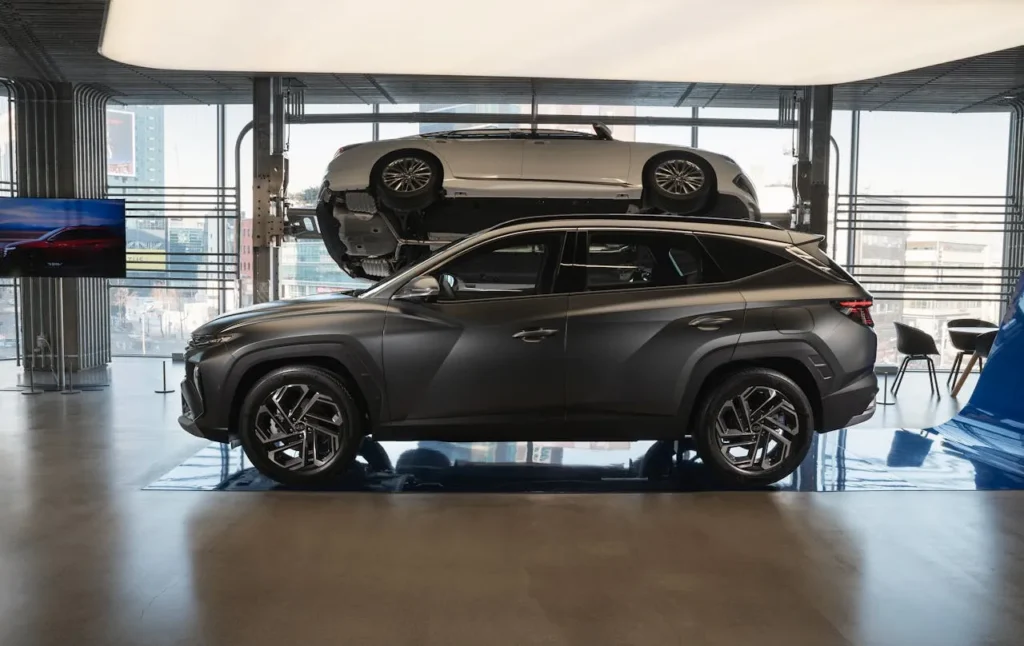 Czarny Hyundai Tucson wystawiony w nowoczesnym salonie samochodowym, na drugim planie auto zamontowane pionowo na ścianie