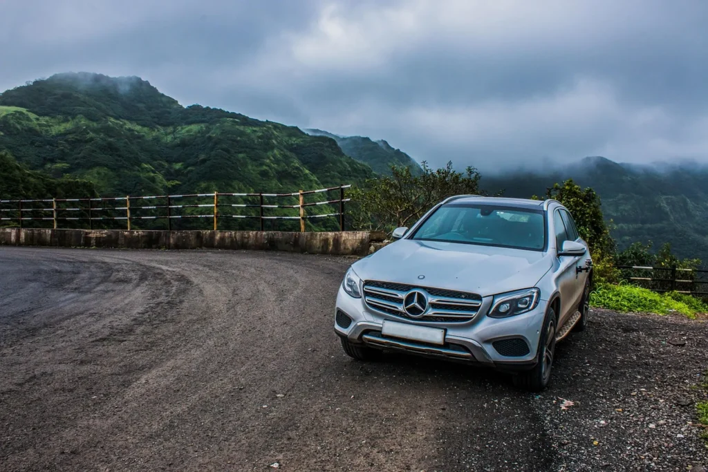 Srebrny Mercedes-Benz GLC zaparkowany na górskiej drodze z widokiem na zielone wzgórza w chmurach