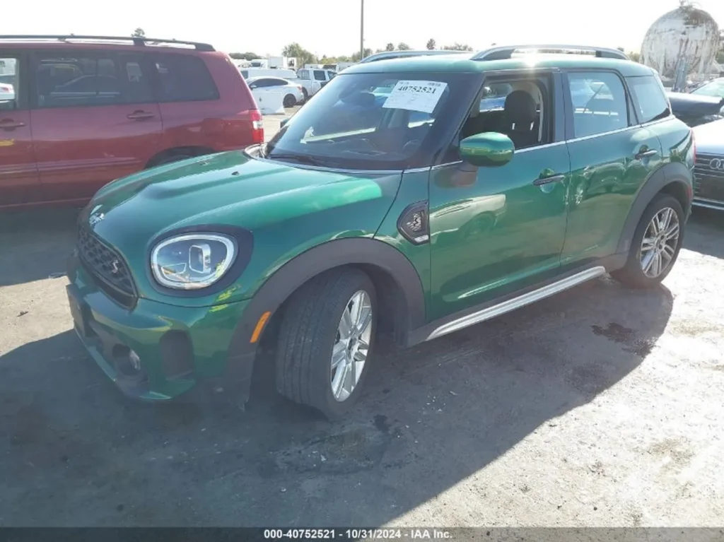 Zielony Mini Countryman S, ujęcie przód-lewy, otwarte okno kierowcy na parkingu.