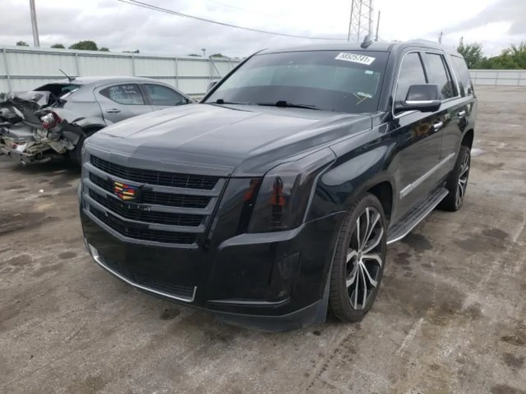 Czarny Cadillac Escalade z przodu z lewej, duże felgi, zdjęcie na placu powypadkowym.