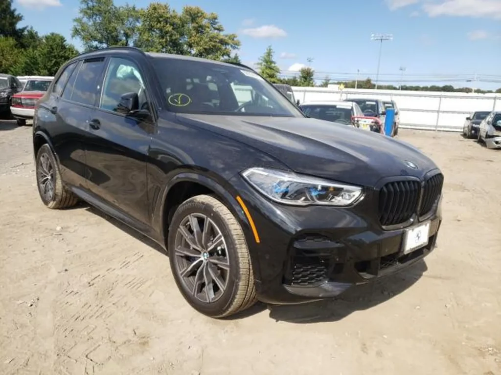 Czarny BMW X5 z przodu z lewej strony, na placu z autami, lakier zakurzony.