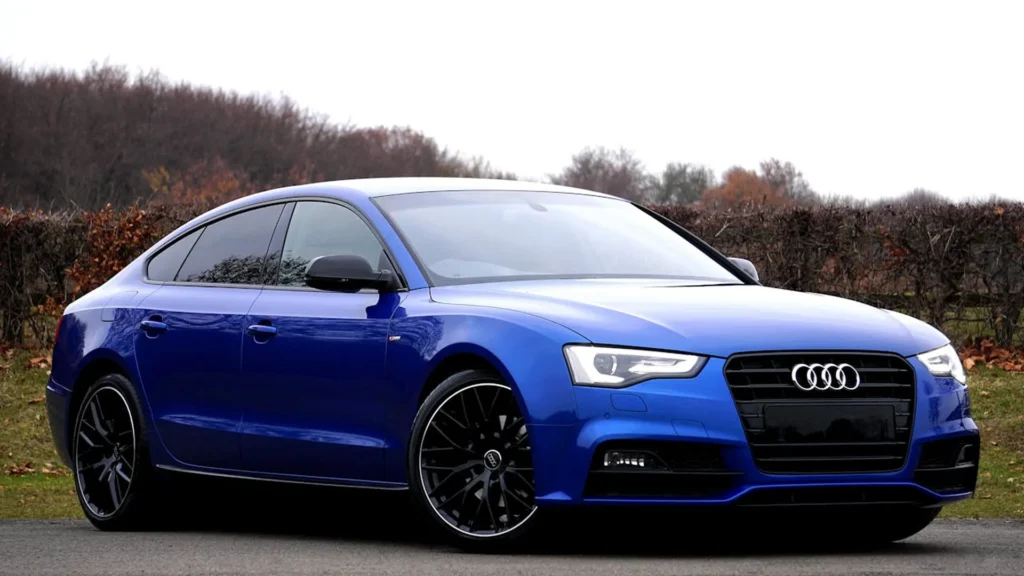 Niebieskie Audi A5 Sportback z czarnymi felgami, ujęcie z boku na tle drzew.