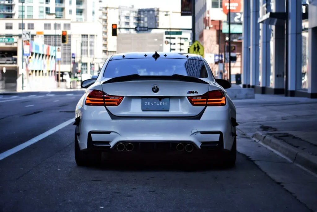 Białe BMW M4 widziane od tyłu na miejskiej ulicy z czterema końcówkami wydechu.