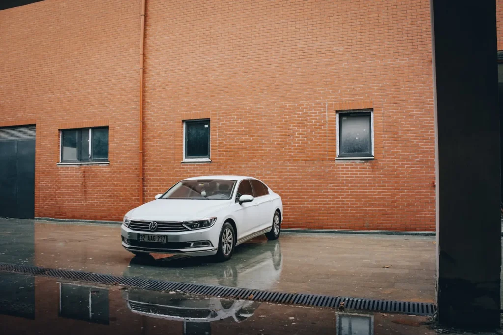 Biały Volkswagen Passat zaparkowany przy ceglanej ścianie po deszczu.