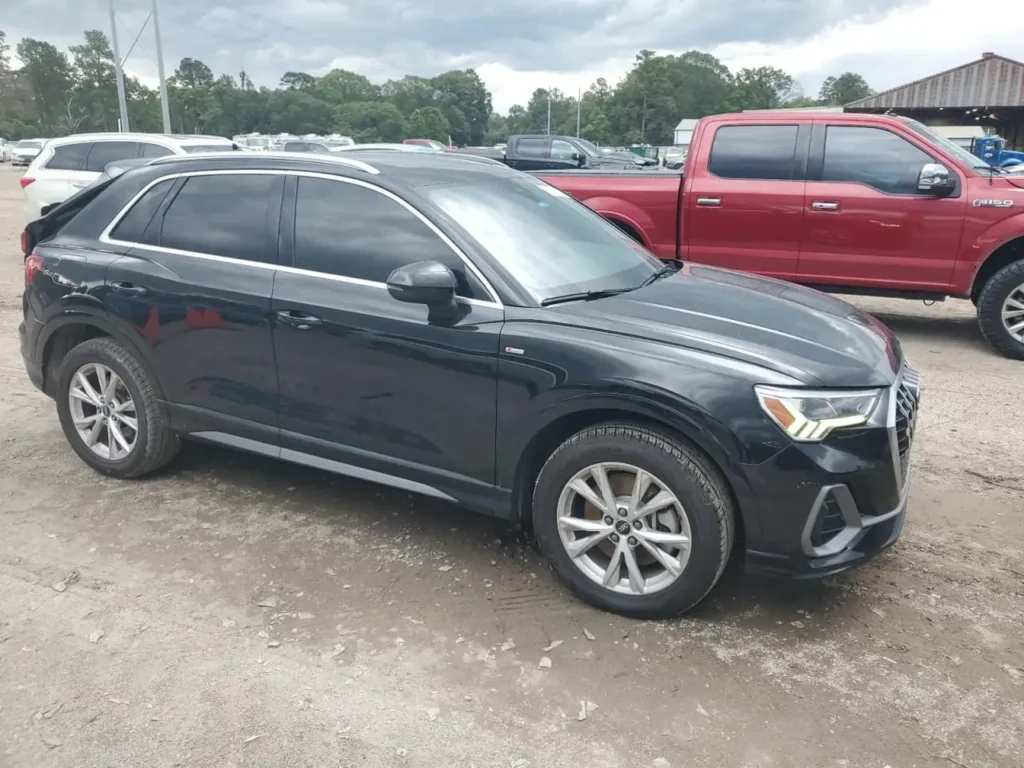 Czarny SUV Audi Q3 S line zaparkowany na szutrowym parkingu, widok z boku