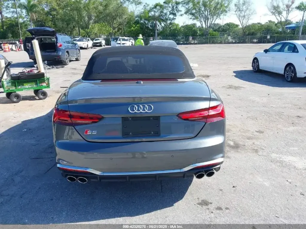 Tył szarego Audi S5 Cabriolet z poczwórnym wydechem na utwardzonym placu.