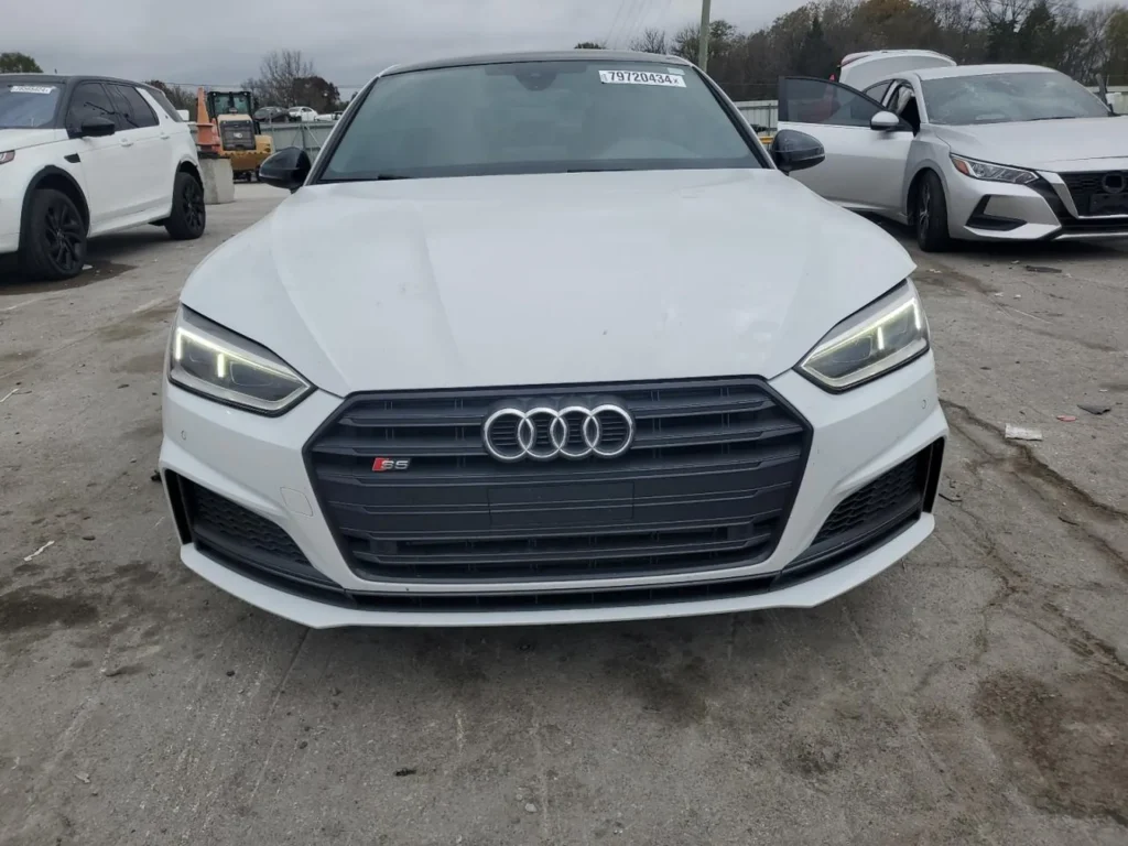 Przód białego Audi S5 Sportback z włączonymi światłami na placu samochodowym