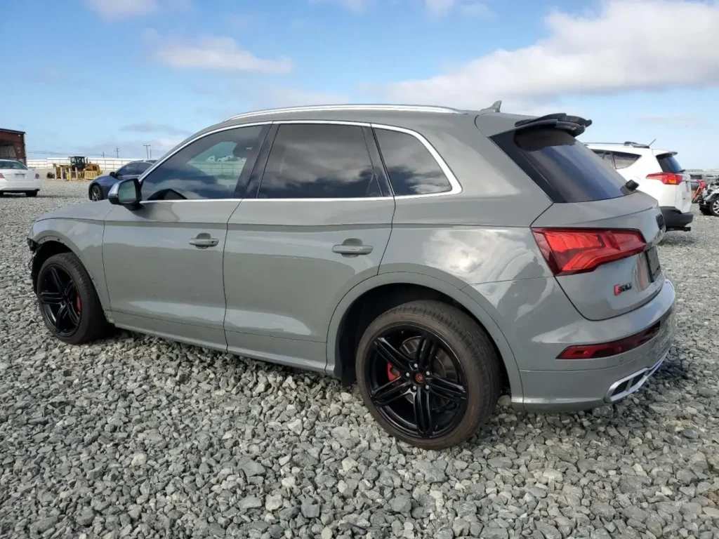 Szary Audi SQ5 z czarnymi felgami widziany z prawego tylnego boku na kamienistym placu