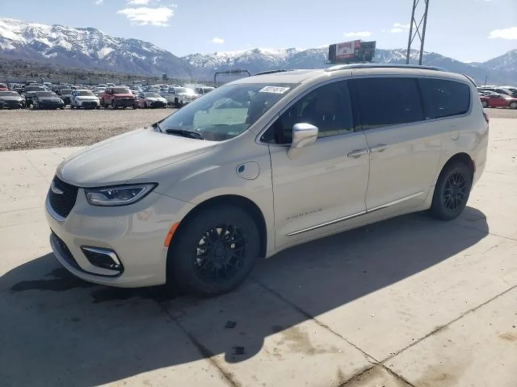Jasny Chrysler Pacifica po liftingu, widok z przodu i boku, zaparkowany na tle ośnieżonych gór.