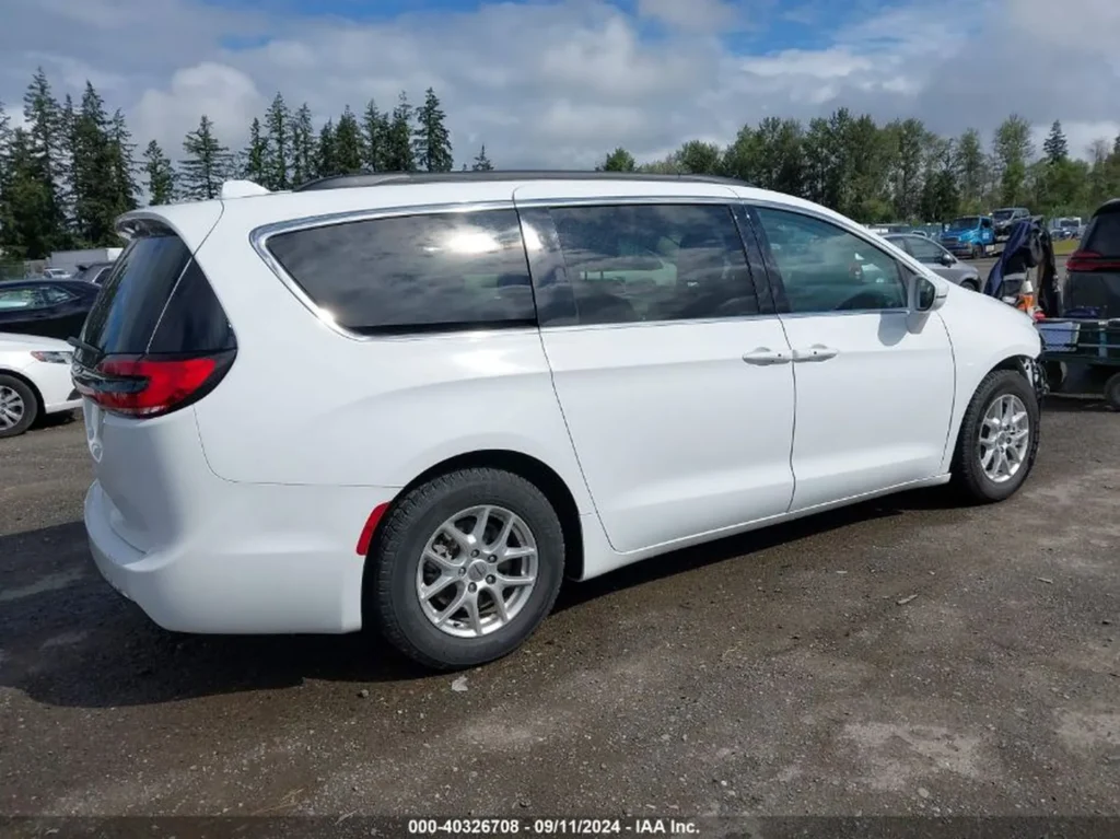 Biały Chrysler Pacifica widziany z prawej strony, stojący na otwartym parkingu.