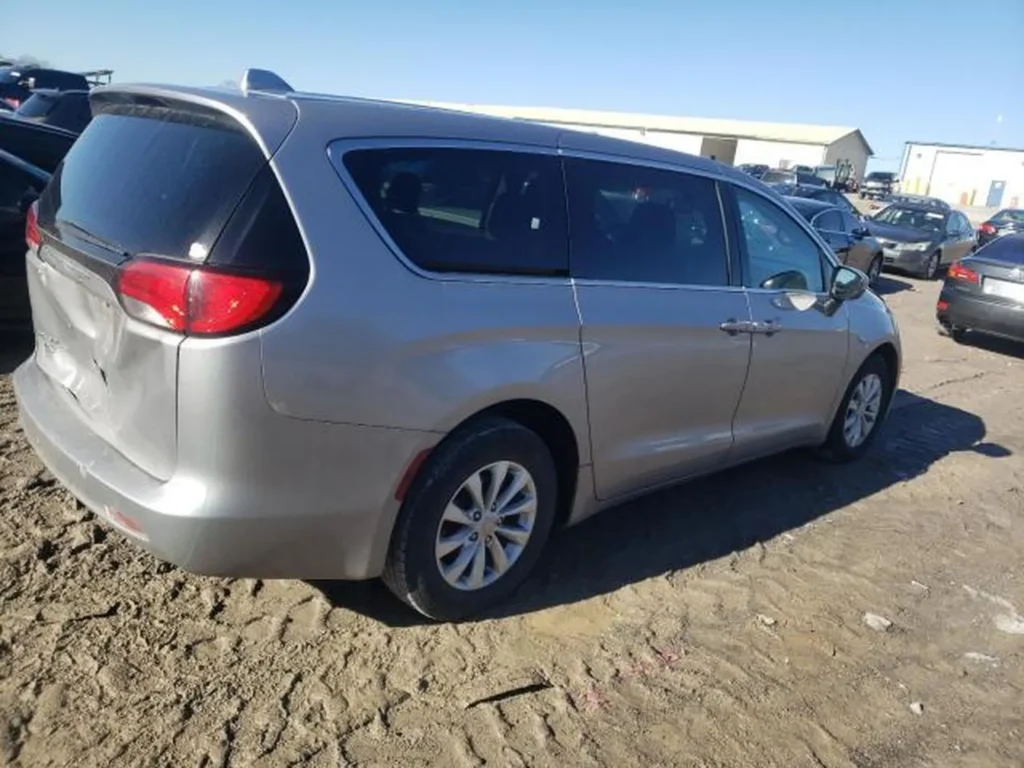 Srebrny Chrysler Pacifica widoczny z prawej strony i tyłu, stojący na piaszczystym placu.