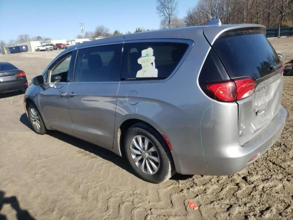 Srebrny Chrysler Pacifica widziany z tyłu i boku, zaparkowany na piaszczystym placu.