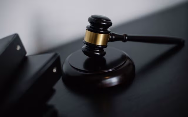 Sędziowski młotek leży na podstawce na ciemnym biurku, symbolizując prawo i rozprawę sądową